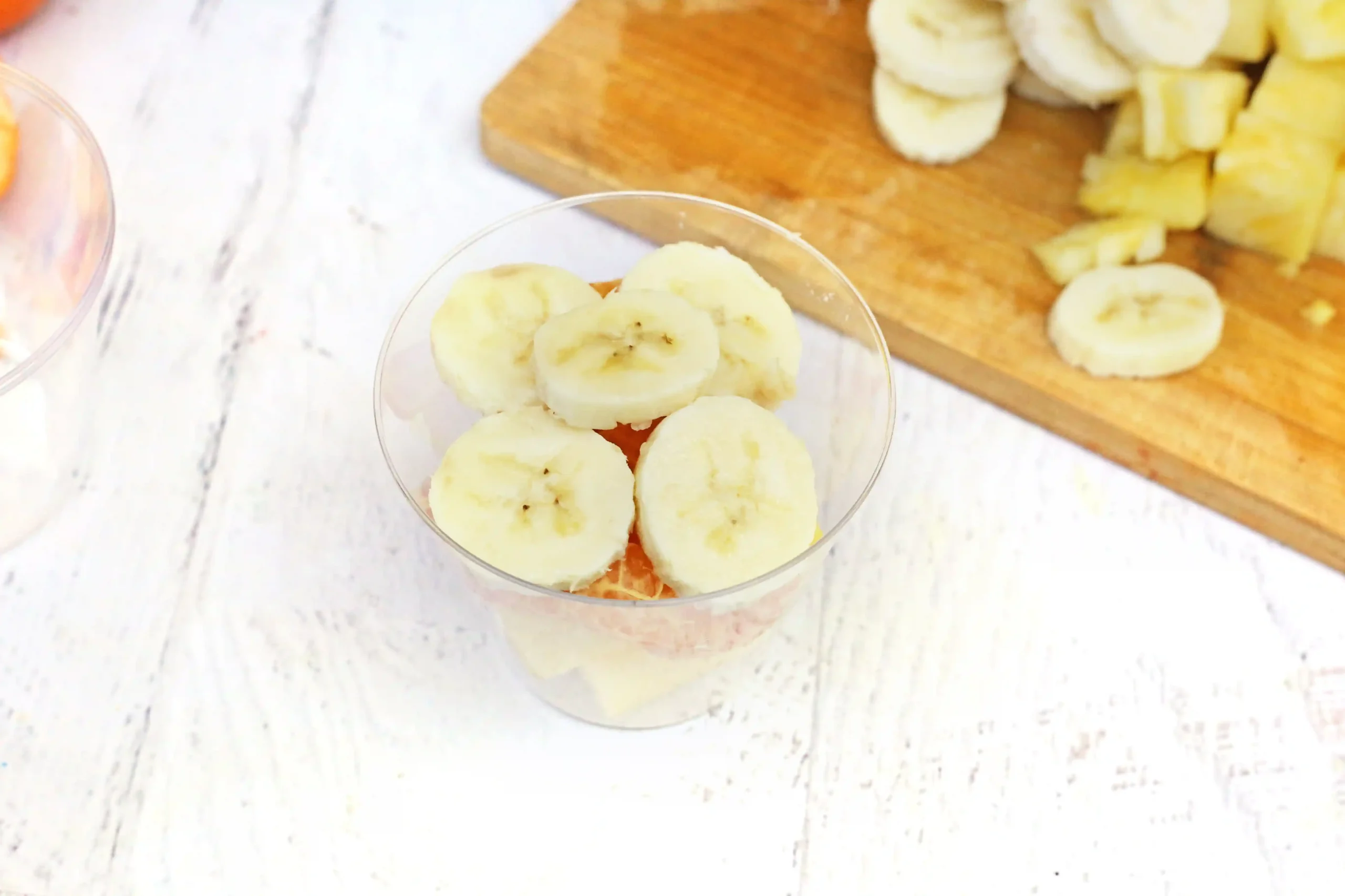 plastic cups with bananas, oranges, and pineapple in them
