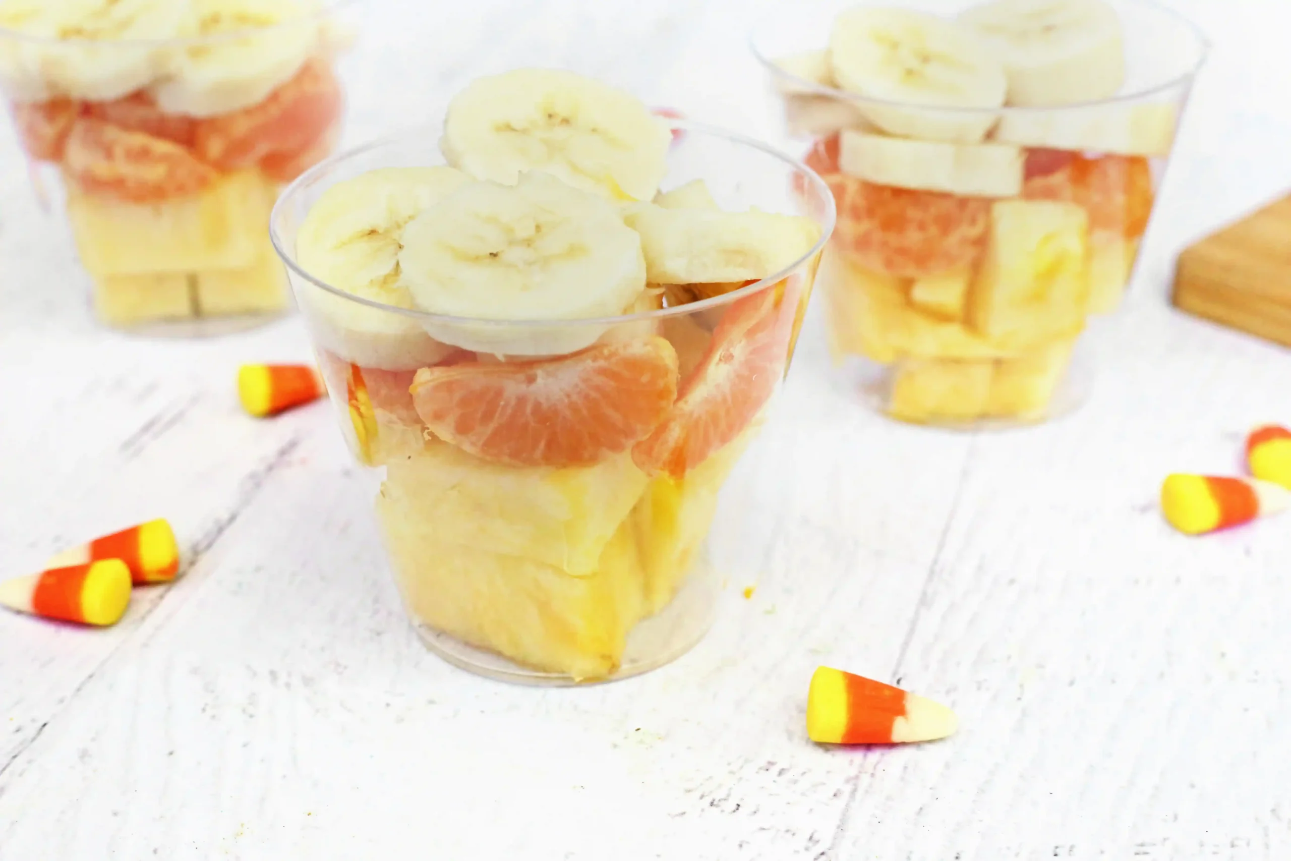 plastic cups with bananas, oranges, and pineapple in them