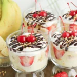 banana split trifle in a clear glass topped with cherries