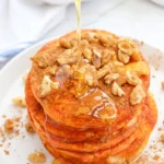 pumpkin pancakes with syrup and walnuts on a white plate