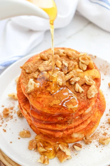 pumpkin pancakes with syrup and walnuts on a white plate