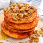 pumpkin pancakes with syrup and walnuts on a white plate