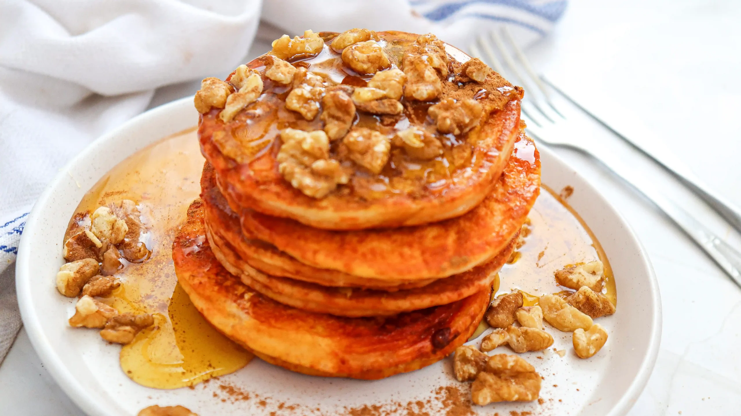 pumpkin pancakes with syrup and walnuts on a white plate