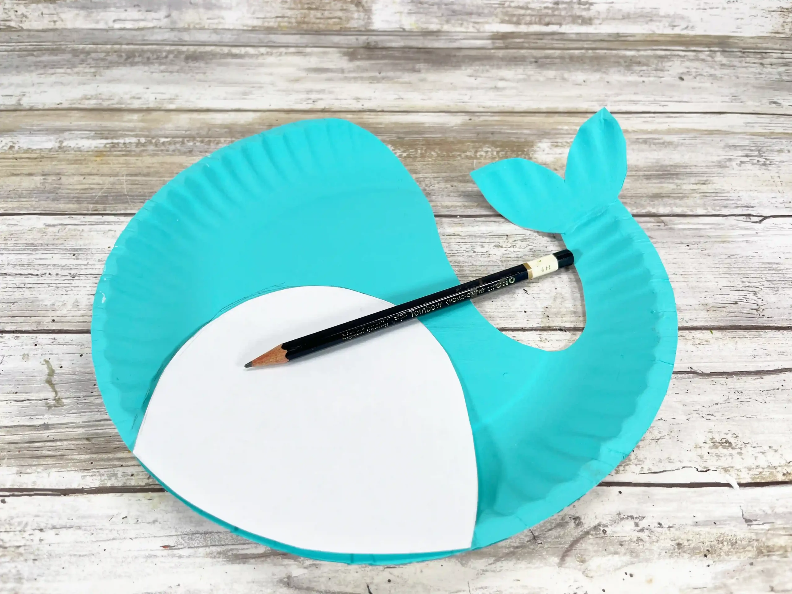 a blue paper plate cut to look like a narwhal with a white piece of paper and a pencil on top