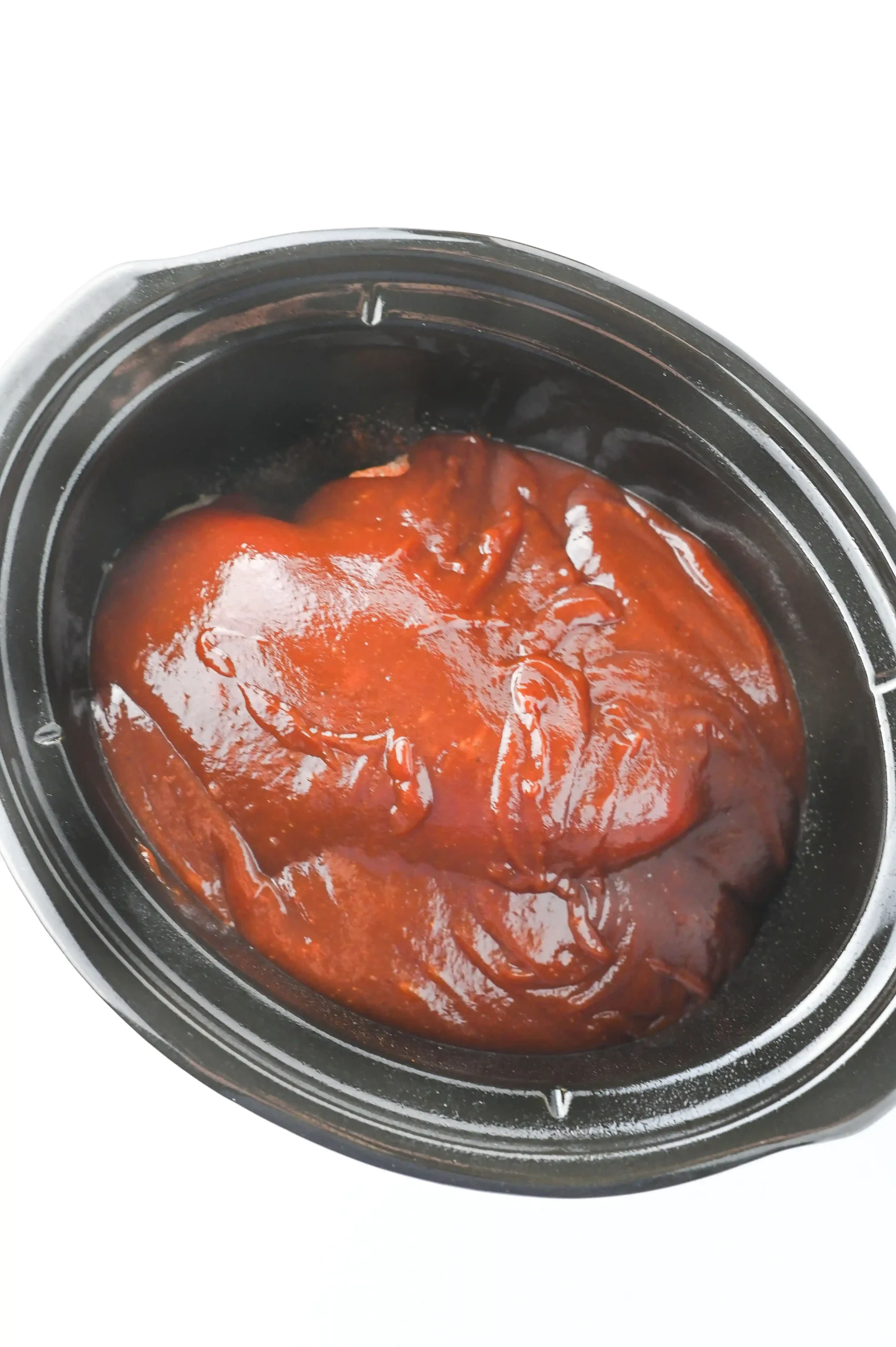 a crockpot with chicken breasts, spices, and barbecue sauce